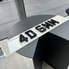 A 4D 6mm number plate with raised black acrylic characters on a white plate, resting on a dark, circular table.