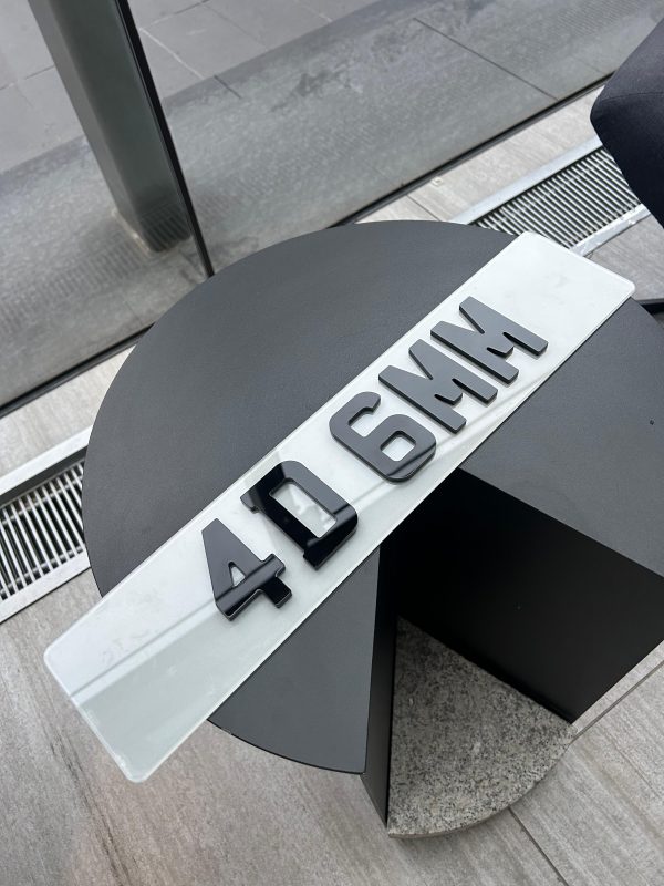 A 4D 6mm number plate with raised black acrylic characters on a white plate, resting on a dark, circular table.