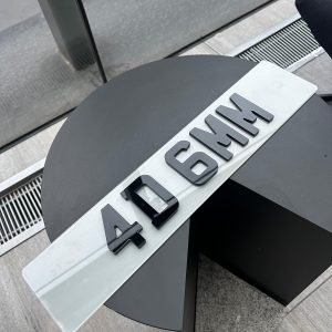 A 4D 6mm number plate with raised black acrylic characters on a white plate, resting on a dark, circular table.