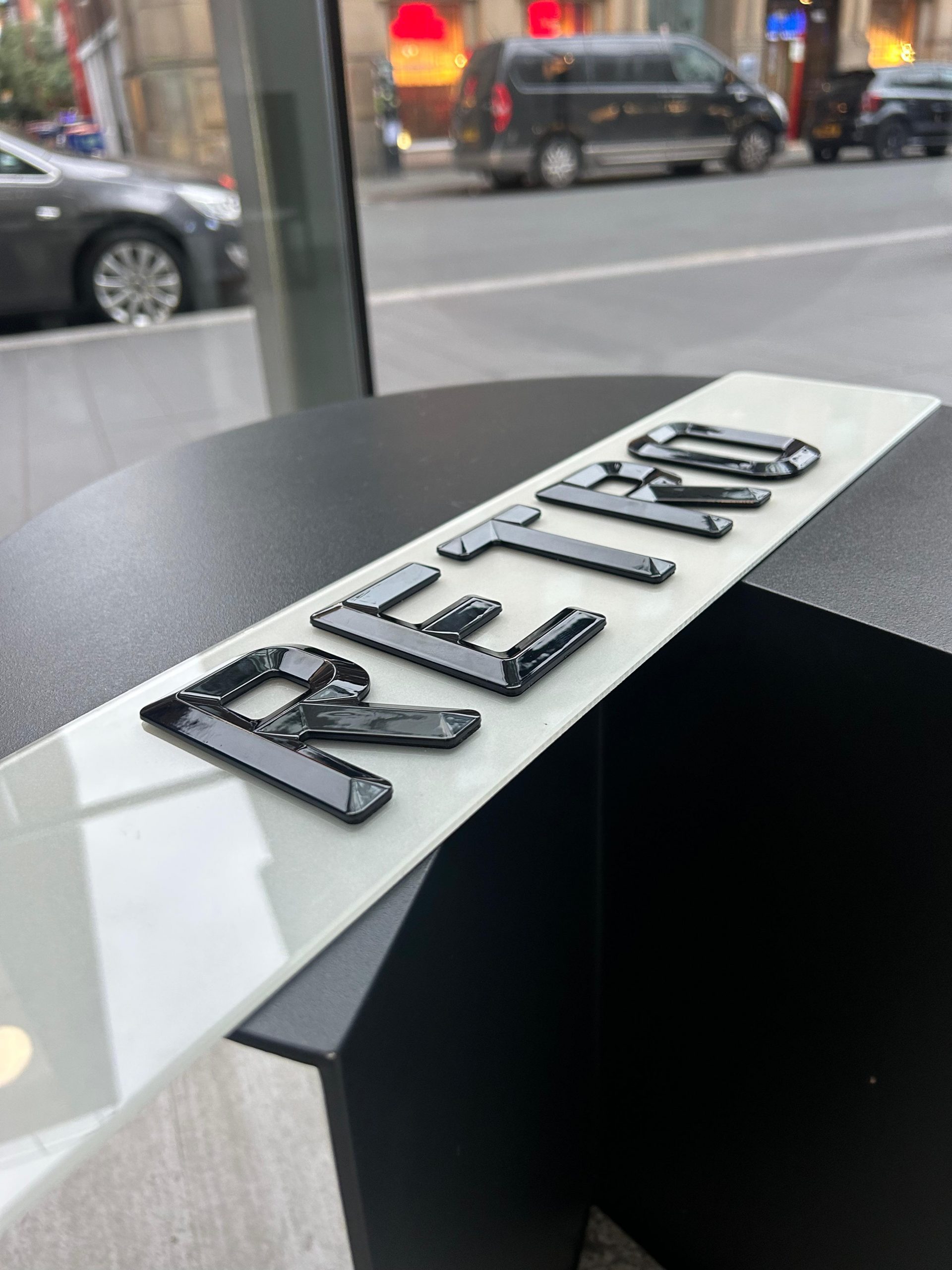 RETRO number plate, 4D number plates, 3D number plates, custom number plates An angled close-up of a 'RETRO' number plate, showcasing the raised, glossy black characters against a blurred street background.