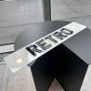A 'RETRO' number plate with glossy, raised black characters on a white plate, resting on a modern, dark table.