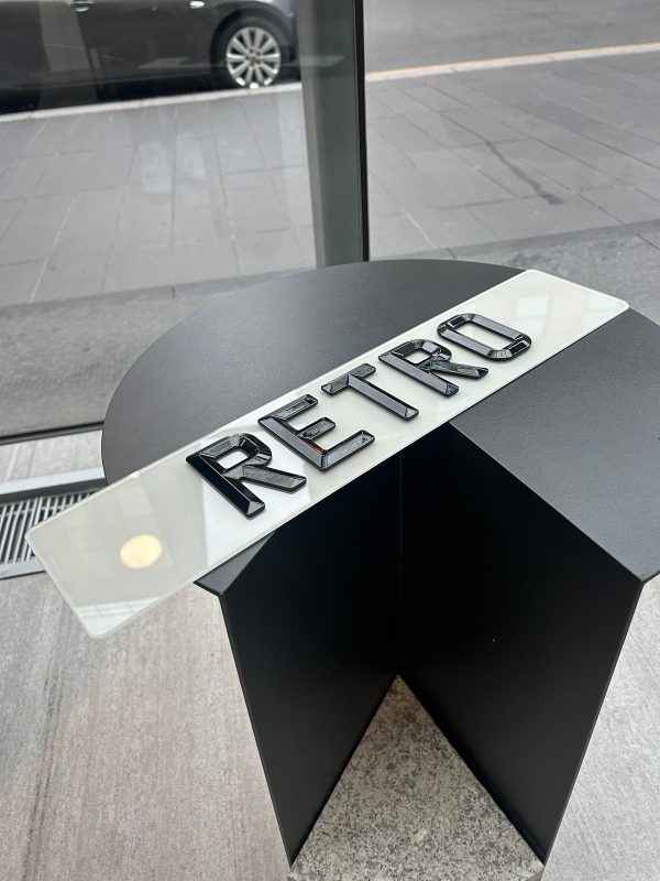 A 'RETRO' number plate with glossy, raised black characters on a white plate, resting on a modern, dark table.