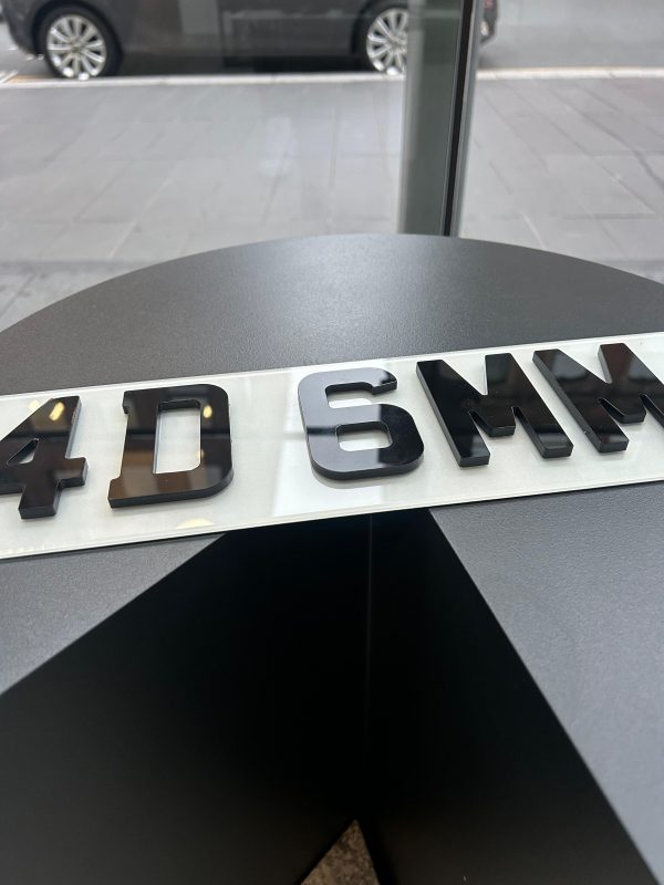 An angled view of a 4D 6mm number plate, showing the raised, laser-cut acrylic characters on a white plate.